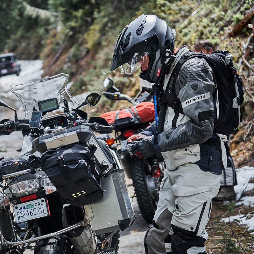 Adventure motorcyclist stands beside his dual purpose motorbike, wearing REV'IT! Dominator 3 GTX apparel