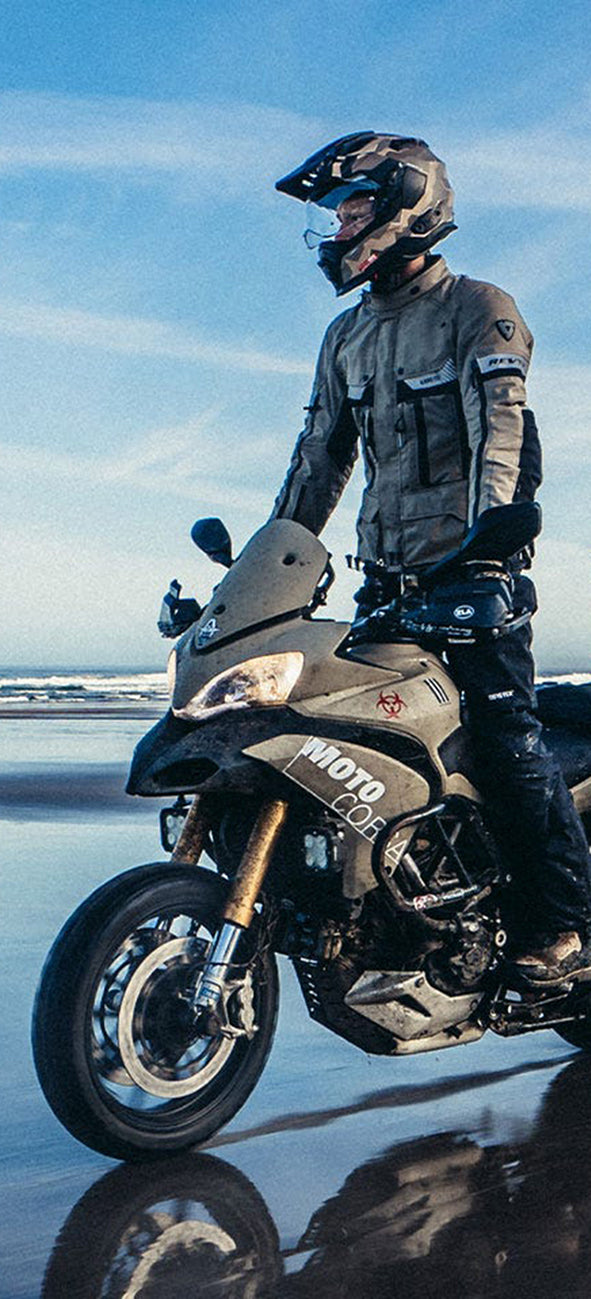 Cropped image of a motorcyclist wearing REV'IT! motorcycle gear, while riding an adventure bike on a beach