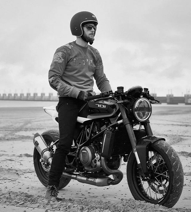 Black and white lifestyle image of a motorcyclist wearing REV'IT! motorcycle jeans, sitting astride his motorbike