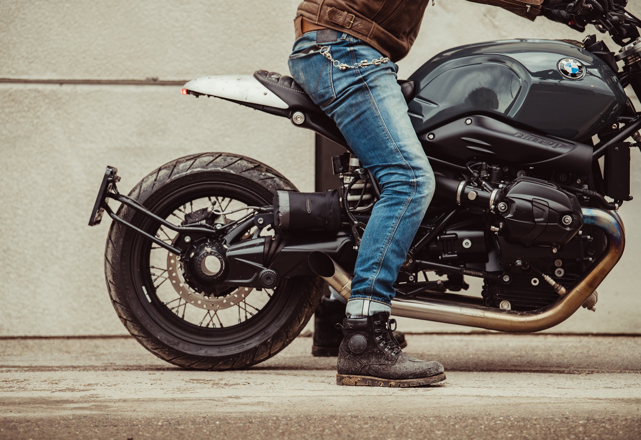 Cropped image of a person sitting astride a motorcycle, with the focus on REV'IT!'s motorcycle jeans and boots