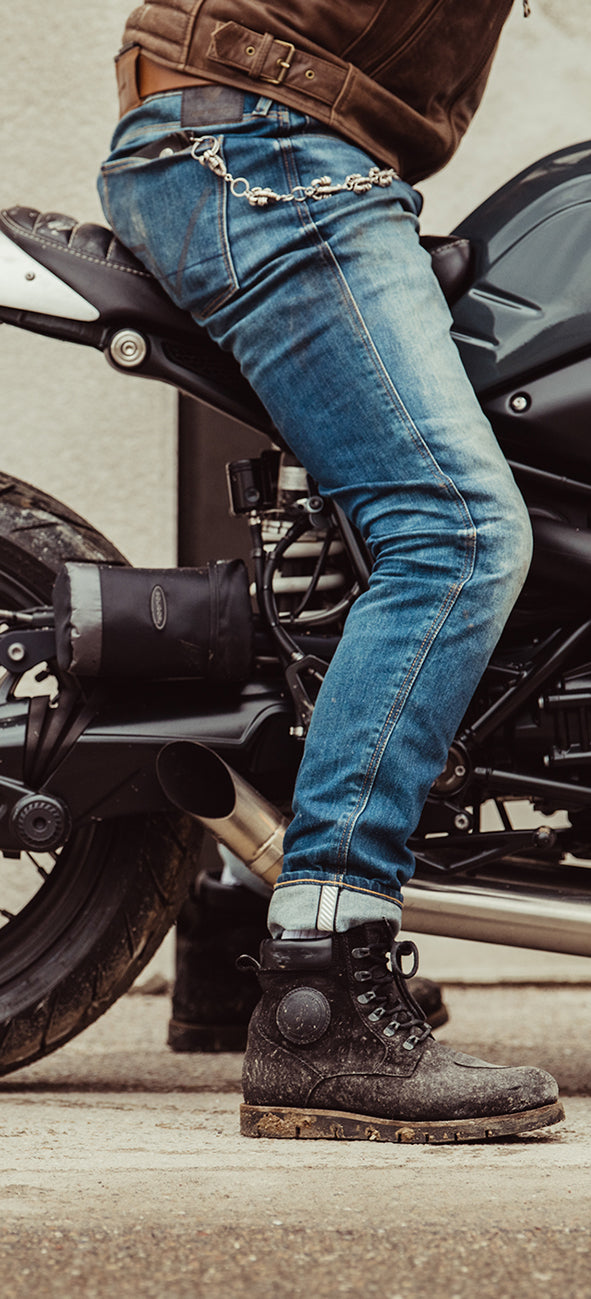 Cropped image of a person sitting astride a motorcycle, with the focus on REV'IT!'s motorcycle jeans and boots