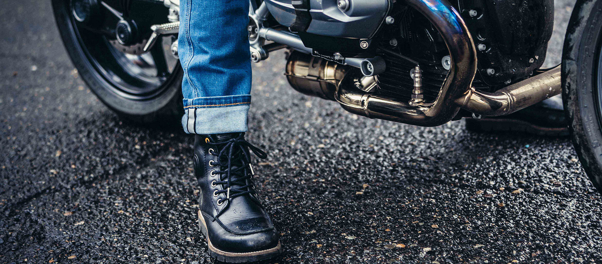 Cropped image of a person sitting astride a motorcycle, with the focus on REV'IT!'s motorcycle footwear